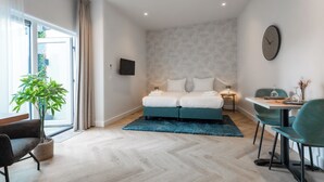 Habitació d'hotel moderna amb llit, taula de menjador, cadira, planta en test i vista a l'exterior.