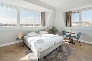 Une chambre moderne avec un lit, des tables de chevet, un bureau et une vue sur la ville.