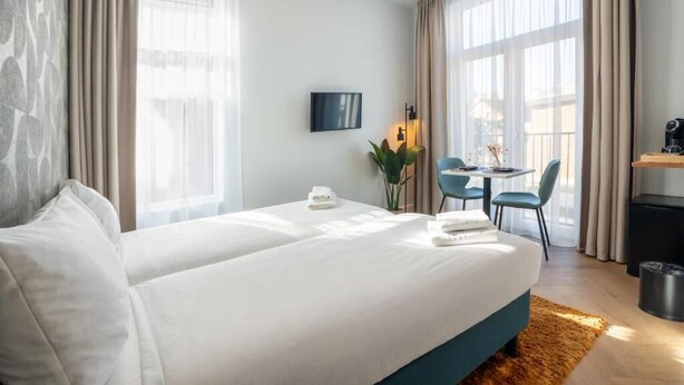 A hotel room with a bed, a desk, a chair, a TV, and a window.