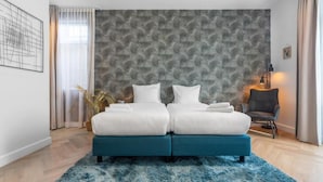A modern bedroom with a double bed, a blue rug, a grey chair, and a patterned wall.