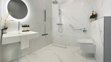 A modern bathroom with a white marble sink, a round mirror, a handheld showerhead, and a toilet.