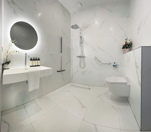 Une salle de bain moderne avec un lavabo en marbre blanc, un miroir rond, une douchette à main et des toilettes.