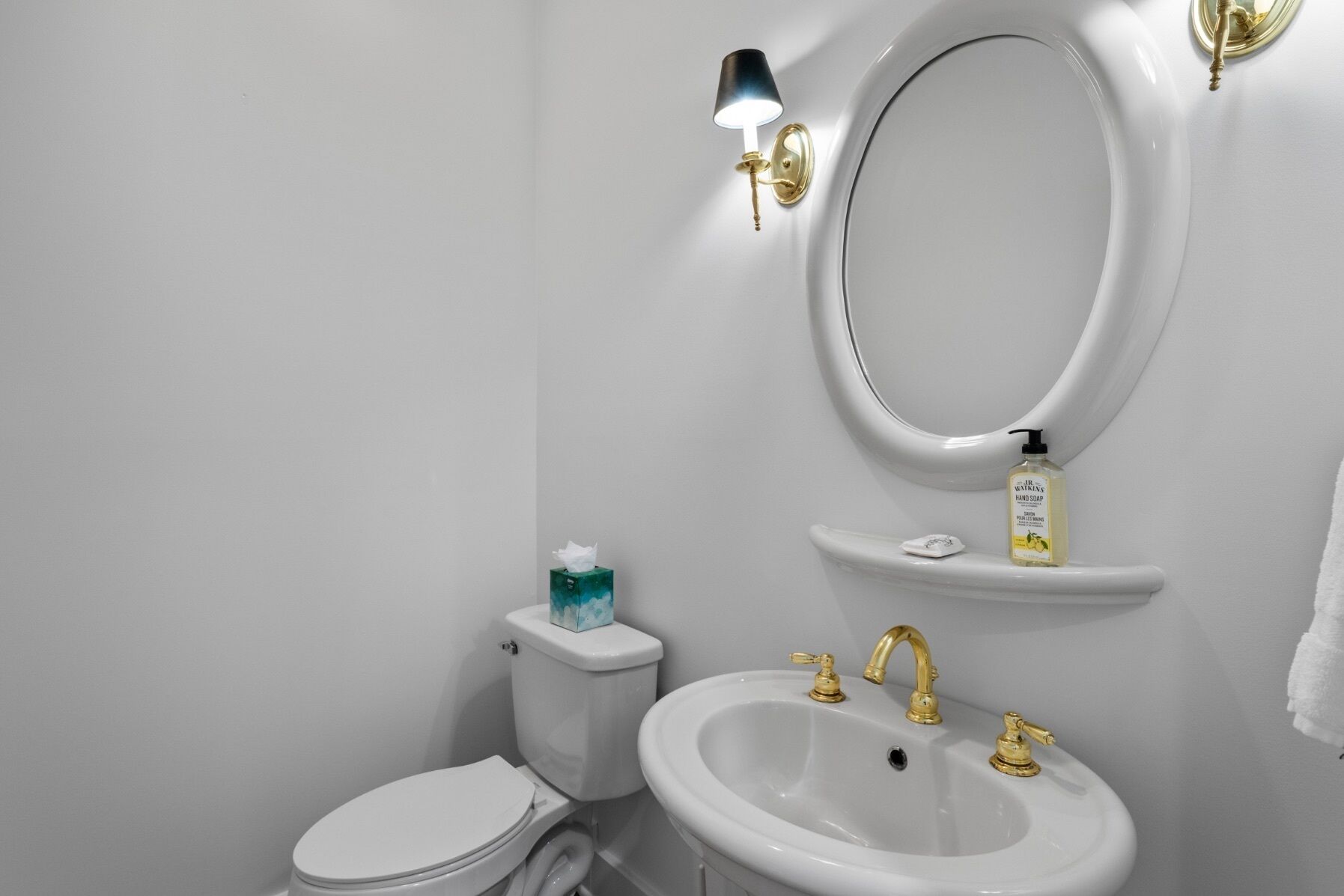 Ein Badezimmer mit Toilette, einem Waschbecken mit goldenen Wasserhähnen, einem Spiegel und einer Seifenspender.