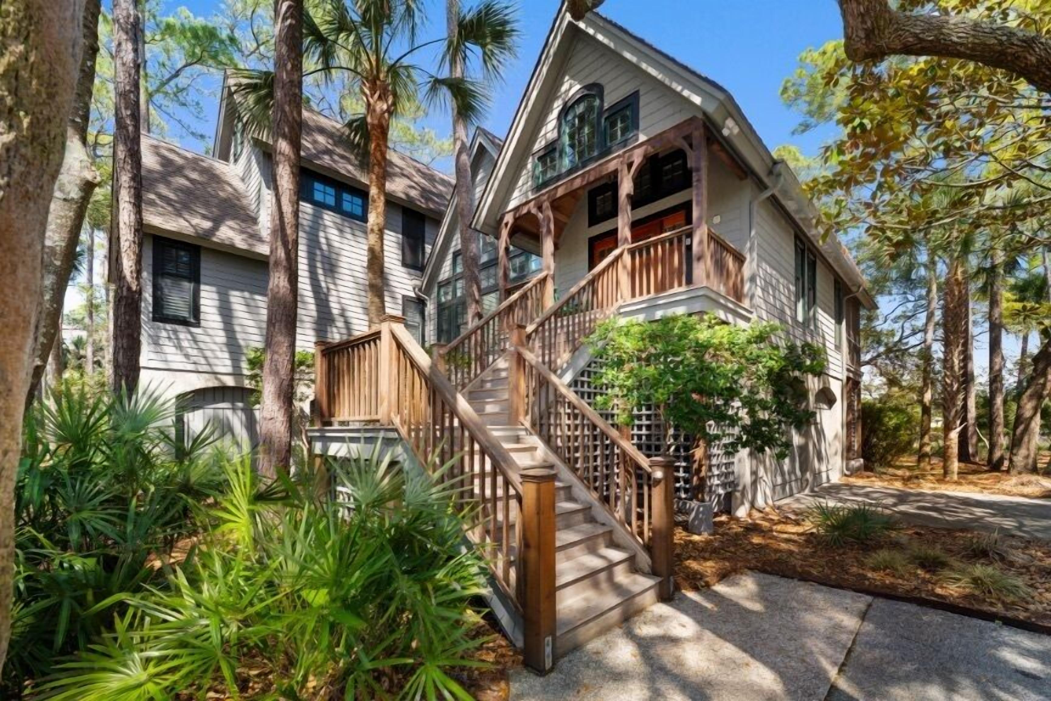 A two-story house with a wooden staircase leading to a balcony, surrounded by trees and greenery.