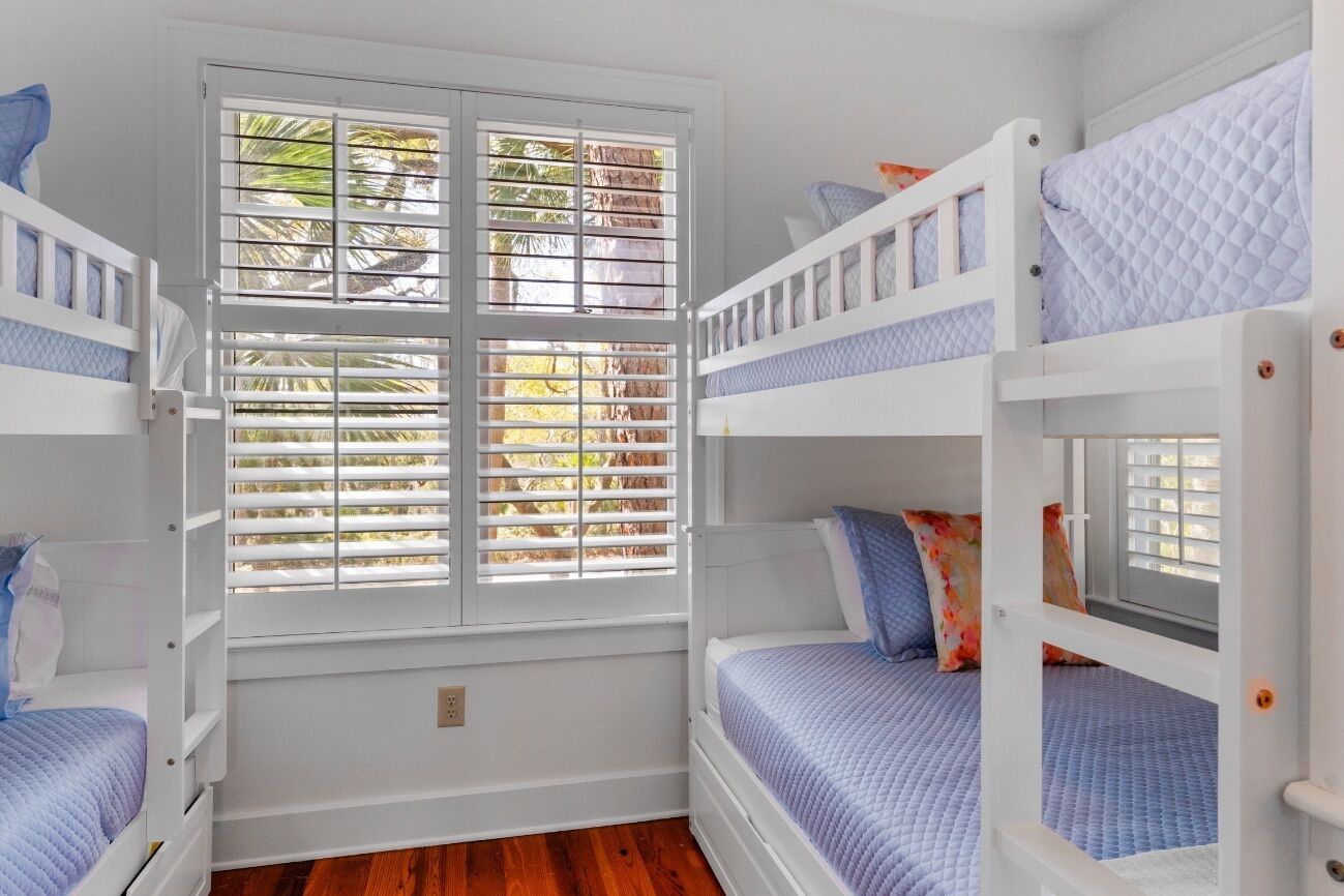 A room with bunk beds, a window with blinds, and a view of palm trees.
