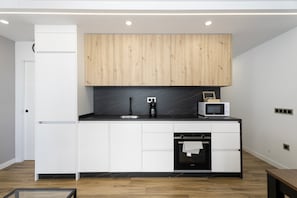 A modern kitchen with white cabinetry, a wooden upper cabinet, a black countertop, a microwave, and an oven. - Vacation Apartment 'Ale Deluxe Home' with Sea View, Wi-Fi and Air Conditioning (Santiago del Teide)