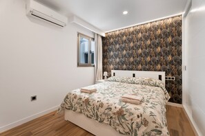 Un dormitorio con cama, ventana, equipo de aire acondicionado y papel tapiz estampado.
