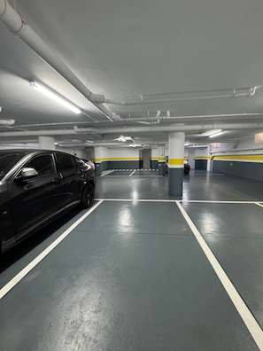 An underground parking garage with multiple parking spaces, concrete pillars, and fluorescent lighting. - Vacation Apartment 'Ale Deluxe Home' with Sea View, Wi-Fi and Air Conditioning (Santiago del Teide)