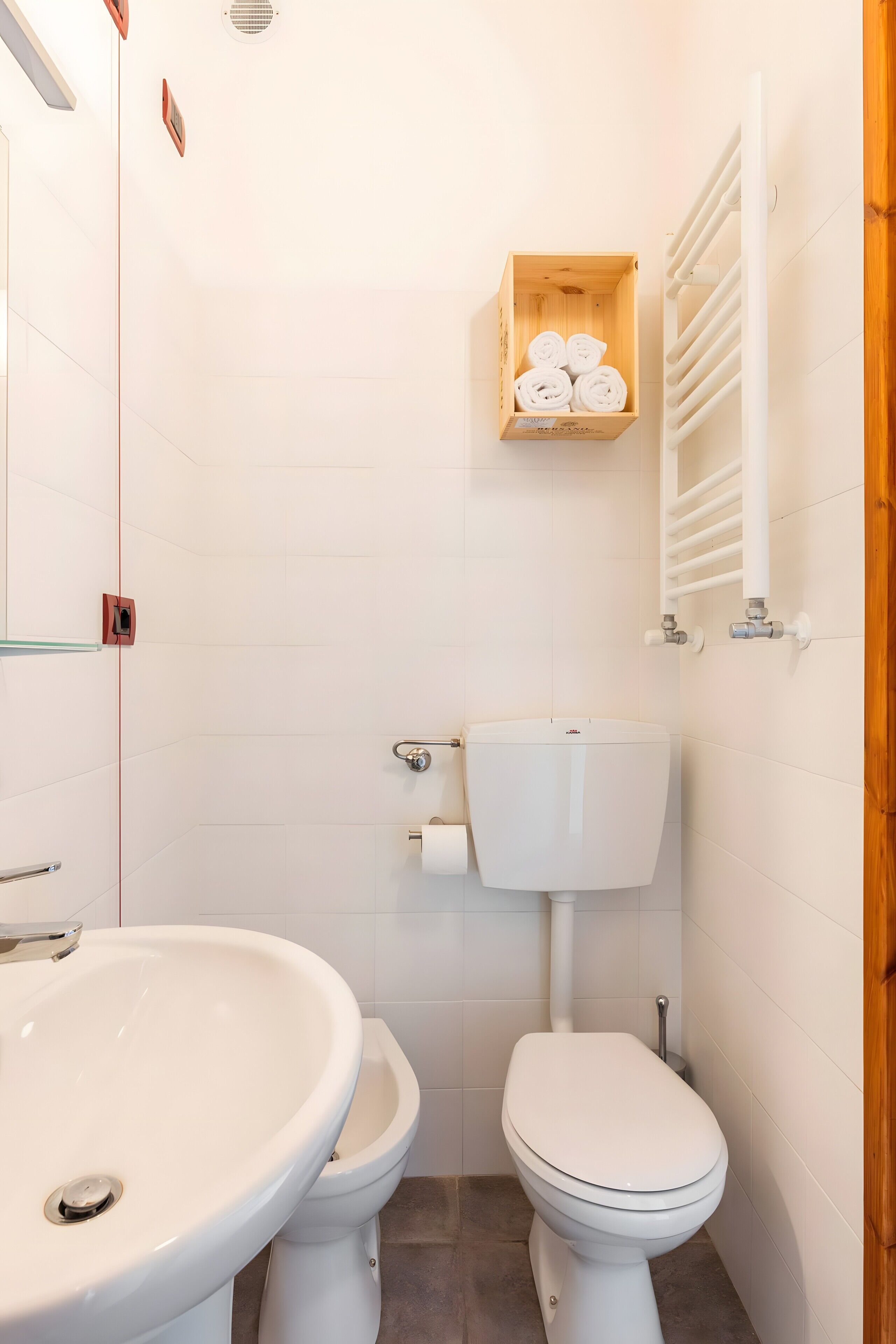 Ein Badezimmer mit weißem Waschbecken, Toilette und Holzregal mit Handtüchern.
