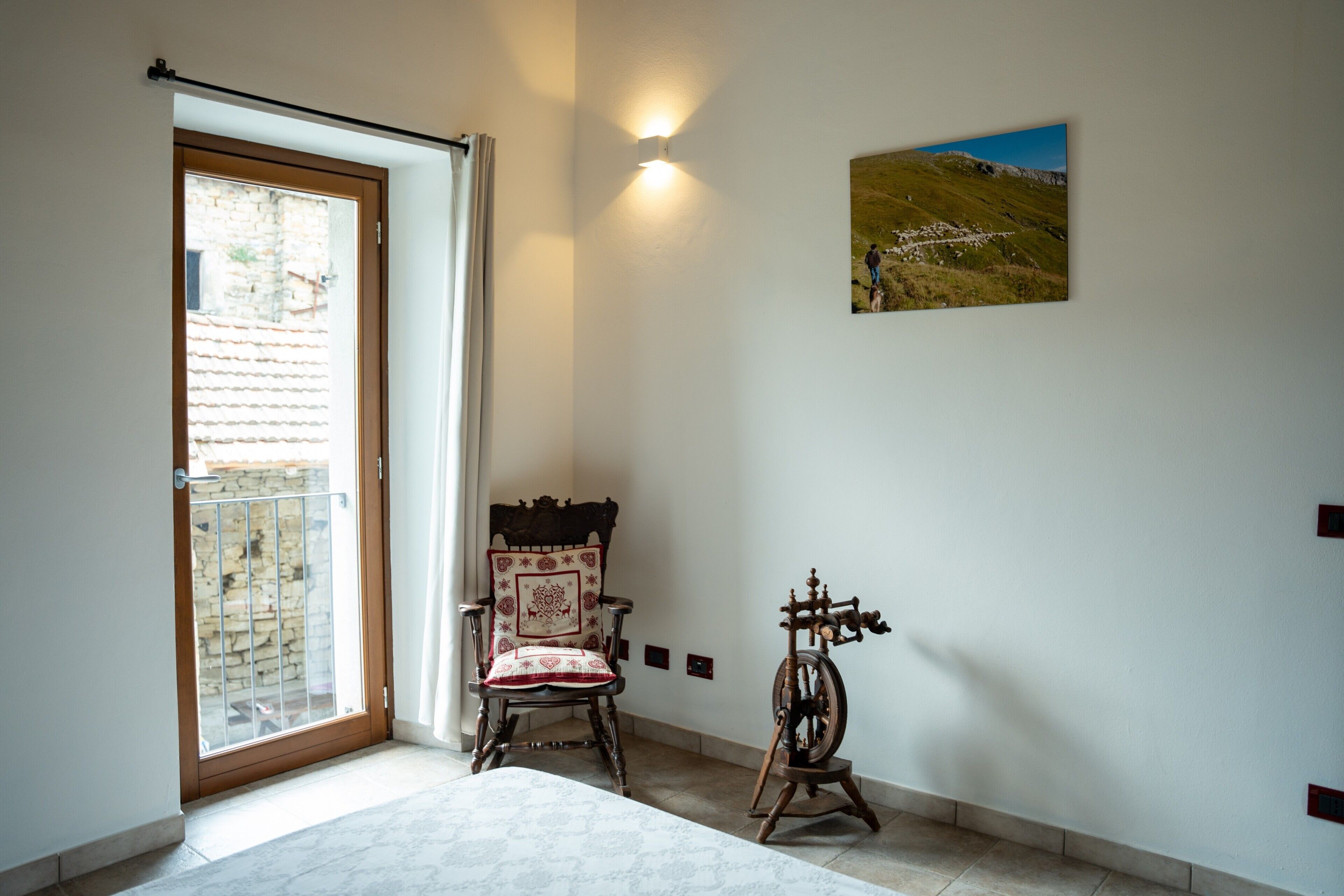 Une pièce comprenant une chaise en bois, un rouet, un tableau accroché au mur et une porte donnant sur un espace extérieur.
