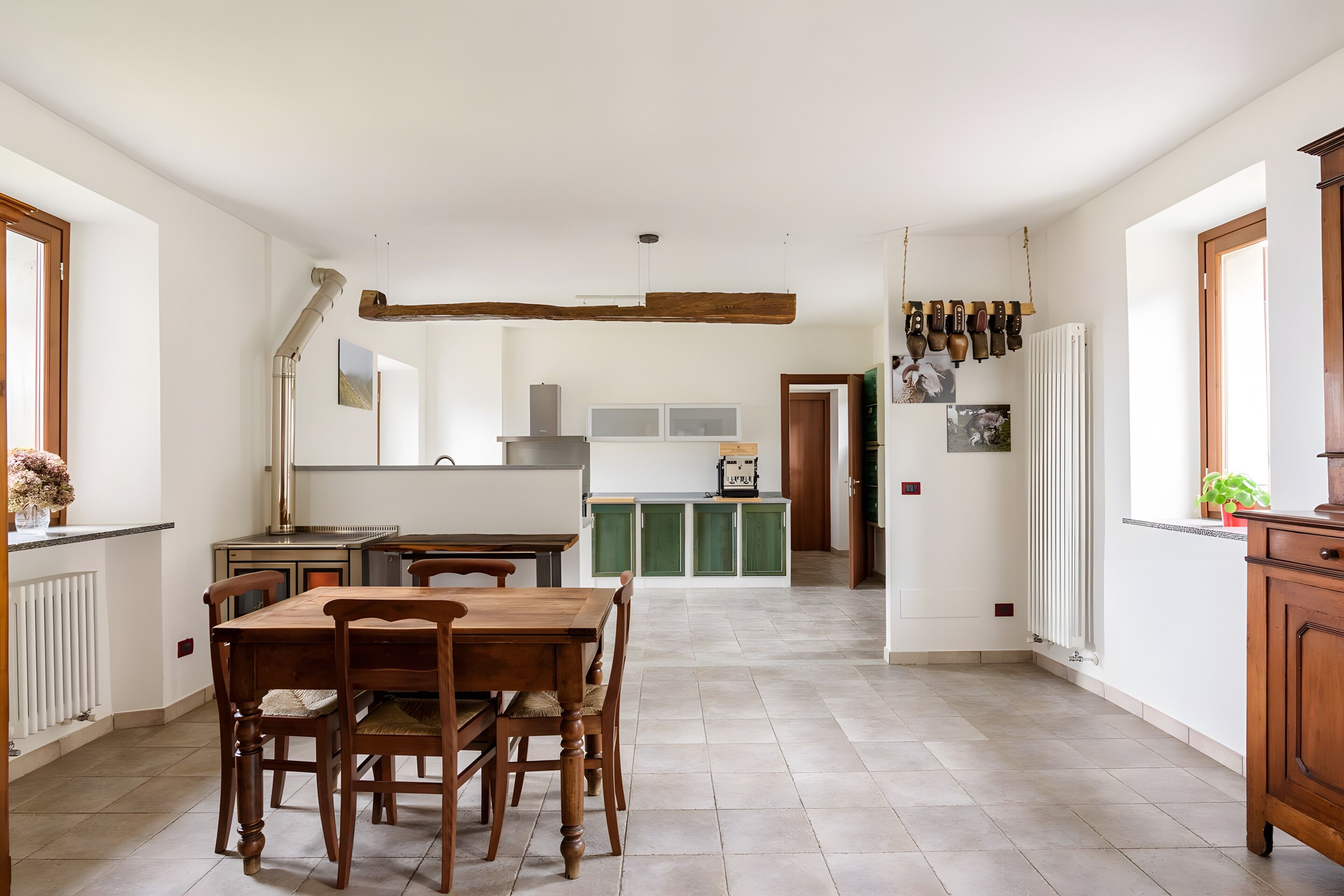 A spacious kitchen with a dining table and chairs, a wooden beam ceiling, and a view into the dining area.