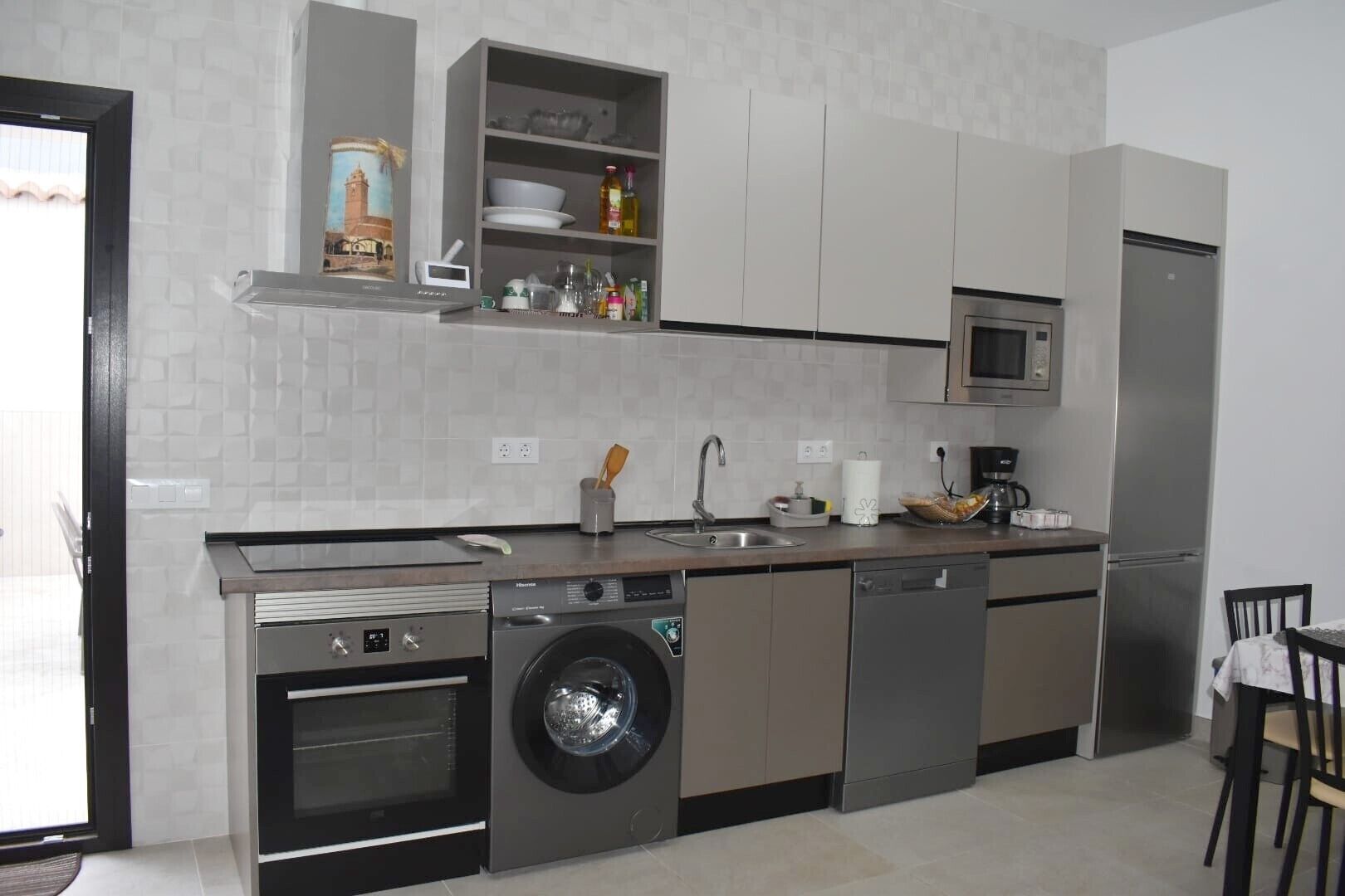 Cocina compacta equipada con lavadora, lavavajillas y microondas, y una pequeña zona de comedor con mesa y sillas.