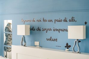 A room with a blue wall, two bedside lamps, a white bedside table, and a decorative quote. - Il Piccolo Nido - One Bedroom Apartment, Sleeps 4 (Florence)