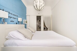 A bedroom with a bed, a blue accent wall, a white ceiling, and a visible laundry area.