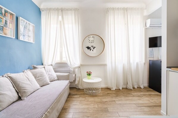 A modern living room with a sofa, a round side table with a flower vase, a small round table, and a wall-mounted TV.