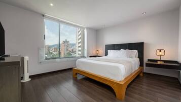 A modern bedroom with a large window, a wooden bed frame, and a nightstand with a lamp.