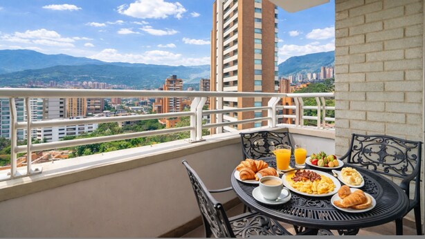 A balcony with a table set for breakfast, a cityscape view, and a tall building in the background. - Poblado de Alejandr a - 1201 (Medellín)