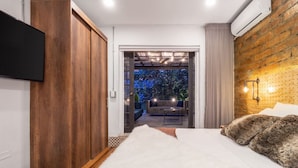 A bedroom with a bed, a TV, a wooden wardrobe, and a view of an outdoor seating area. - Casa Madera Parque Lleras With Private Jacuzzi (Medellín)