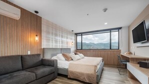 Ein modernes Hotelzimmer mit Bett, einer Couch, einem Fernseher und einem großen Fenster mit Blick auf die Berge.