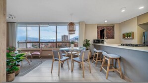A modern kitchen with a dining area, large windows, and a city view. - Alcazar Oviedo - 1103 (Medellín)