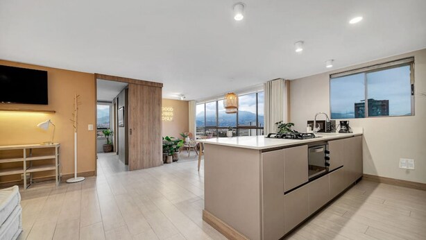 A modern kitchen with a central island, built-in appliances, and large windows offering a city view. - Alcazar Oviedo - 1103 (Medellín)