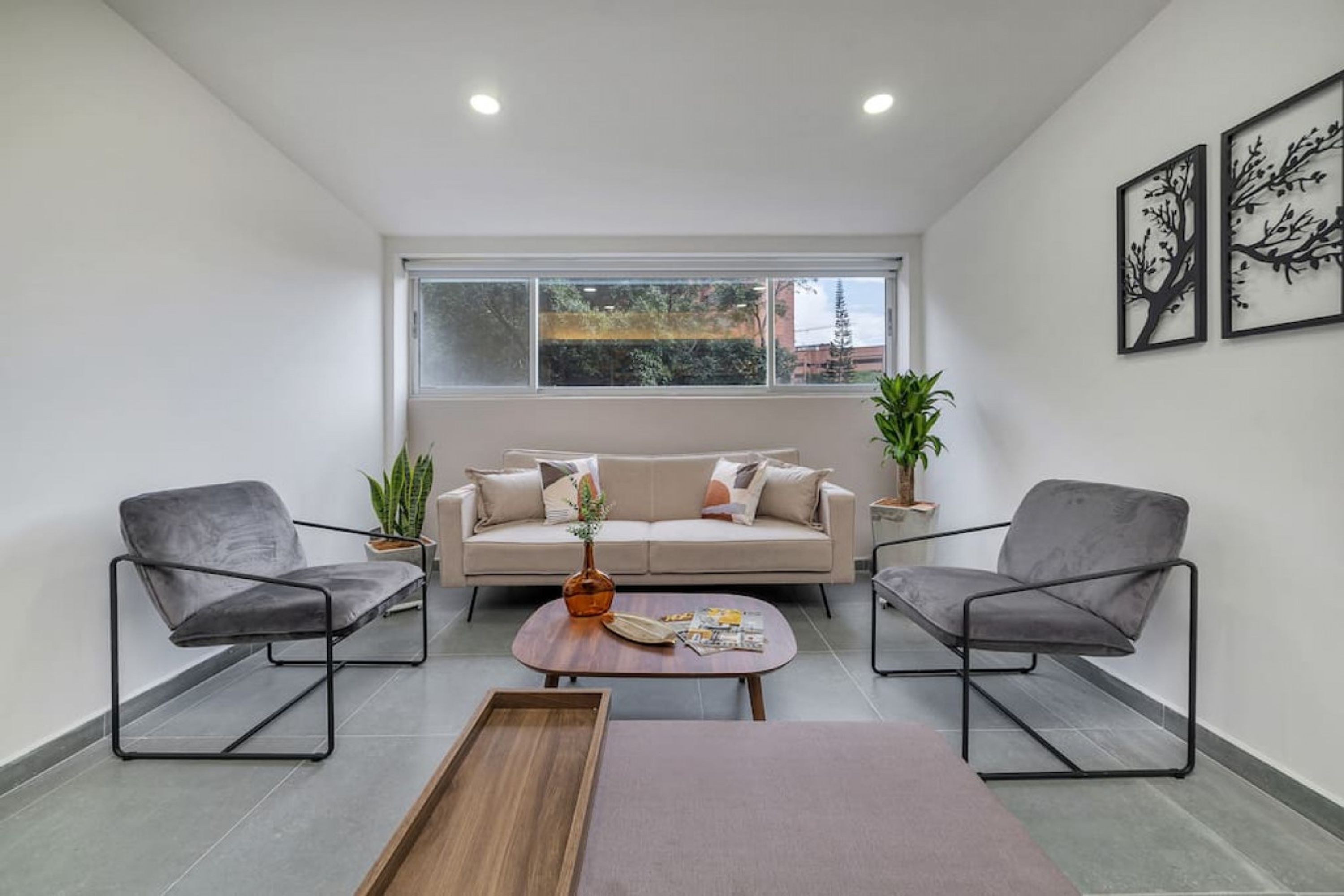 A modern living room with a sofa, two armchairs, a coffee table, and a window with blinds.