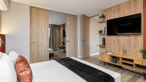 A modern hotel room with a bed, a TV, wooden paneling, a desk, and a wardrobe. - Go Living Suites - 807 (Medellín)