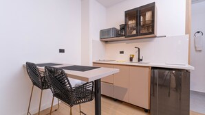 Une cuisine compacte dotée d’un plan de travail blanc, d’un four à micro-ondes, d’une machine à café et d’un lave-vaisselle. On y trouve deux chaises noires au design tissé.