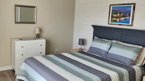 Een slaapkamer met een bed, een dressoir, een stoel, een lamp en een schilderij aan de muur.