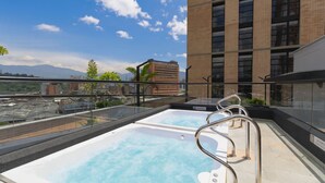 A rooftop pool with clear blue water, surrounded by glass railings, and a view of a tall building and mountains in the background. - Metropolitan Living - 515a (Medellín)