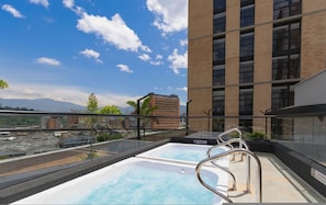 Una piscina en la azotea con barandas de metal, cielo despejado y vista a la montaña.