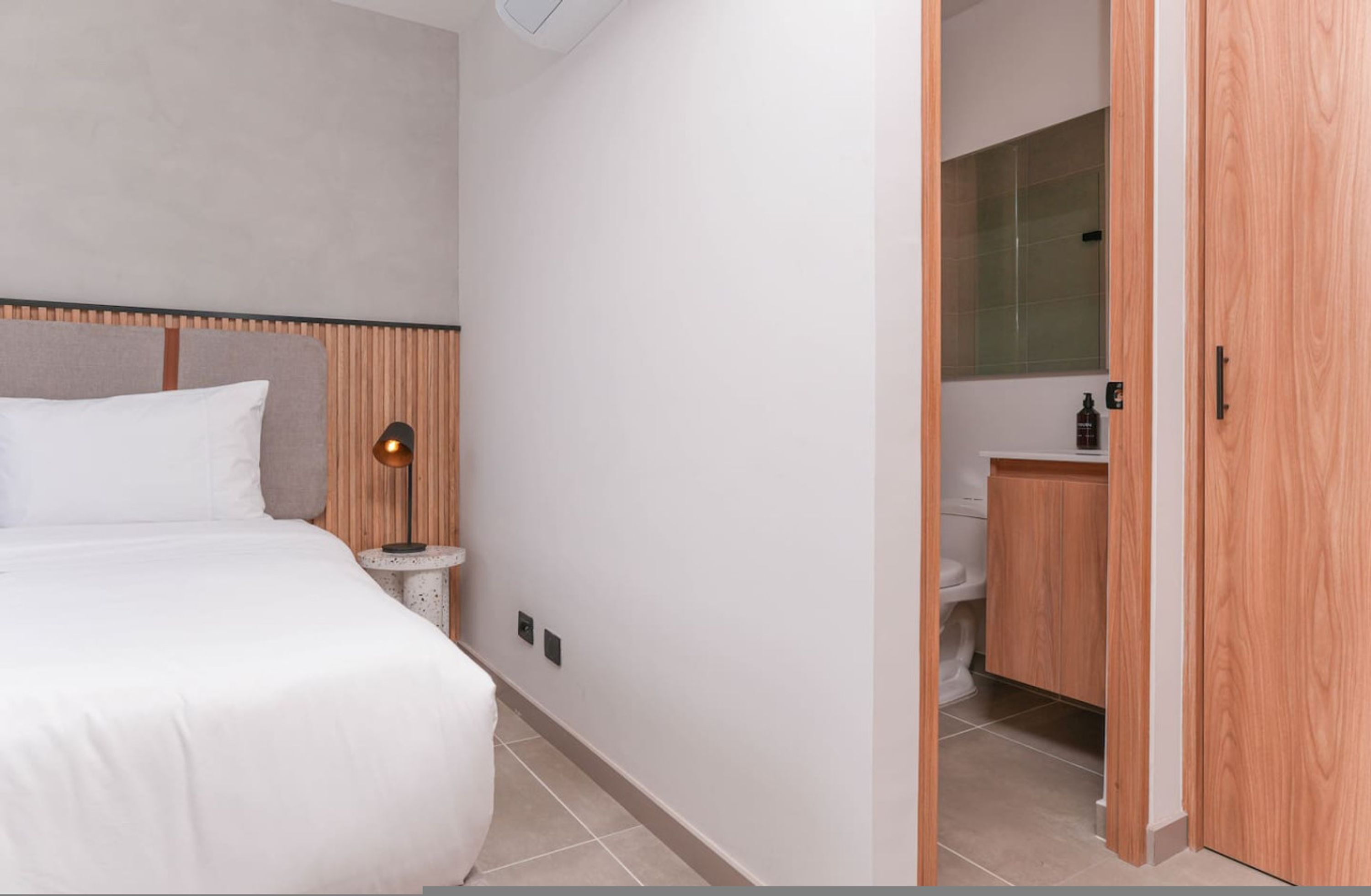 Una camera d'albergo con un letto, comodino, lampada e vista sul bagno.