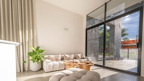 A modern living room with a sofa, two wooden side tables, a large potted plant, and a sliding glass door leading to an outdoor area. - Metropolitan Living - 515a (Medellín)