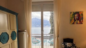 Um quarto com cama, radiador, janela com cortinas, uma cadeira e um quadro.