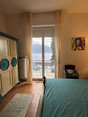 Ein Schlafzimmer mit einem Bett, einem Heizkörper, einem Fenster mit Vorhängen, einem Sessel und einem Gemälde.