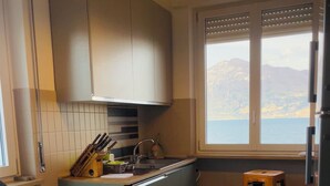 Cozinha compacta com janela, um banquinho e vista para o mar.