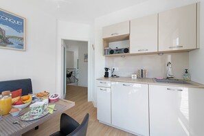 A modern kitchen with white cabinets, a dining table with breakfast items, and a view into the living area.