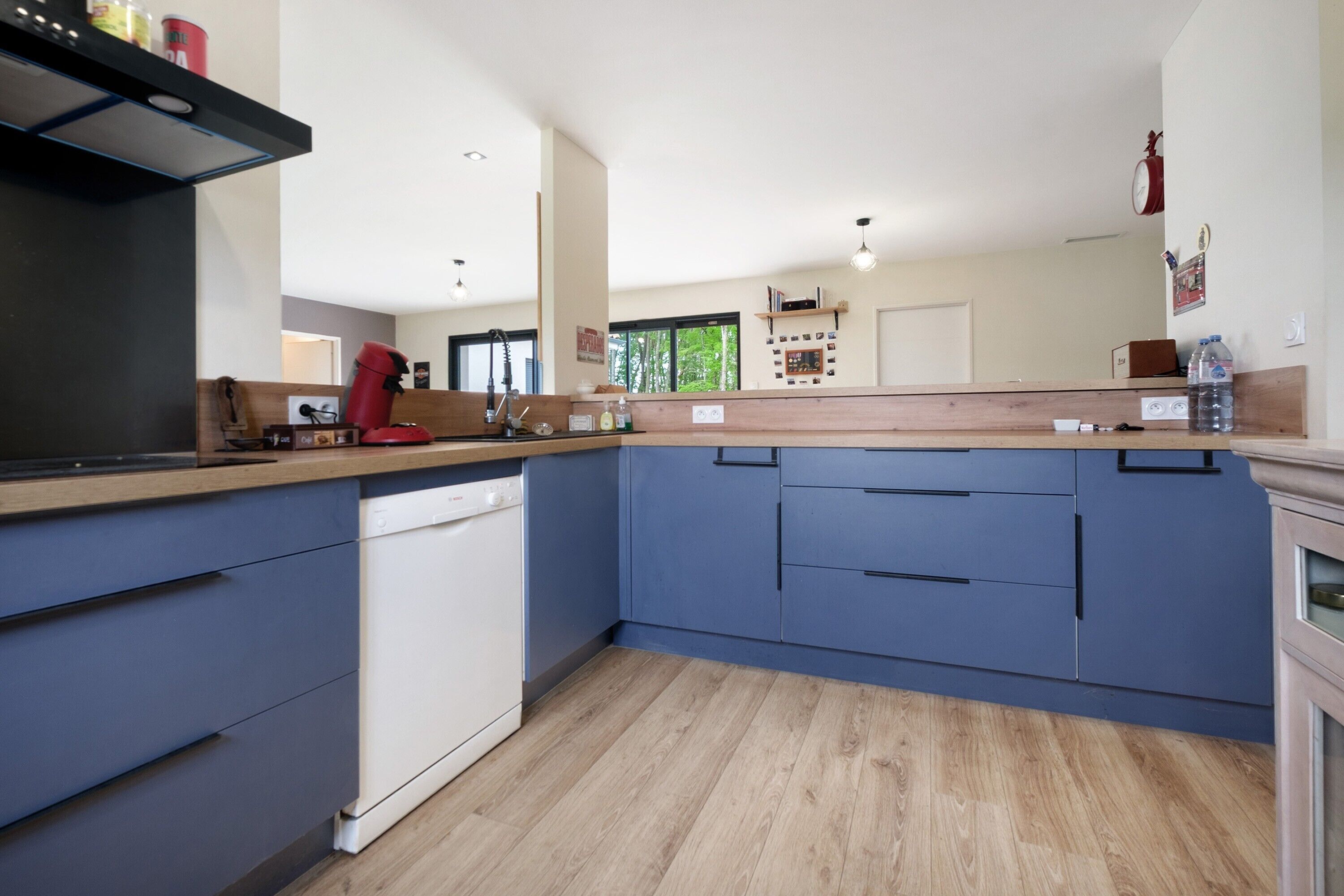 A kitchen with a dishwasher, wooden countertop, blue cabinets, and a red coffee maker.