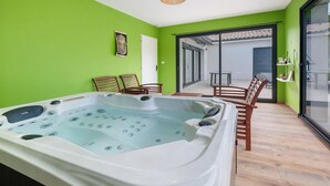 A room with a hot tub, wooden chairs, a glass door leading outside, and a green wall. - Relaxation & Serenity in Coulounieix-Chamiers – House with Pool and Spa (Coulounieix-Chamiers)