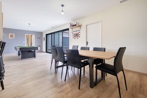 Un espace repas comprenant une table de billard, des chaises noires et une table en bois.