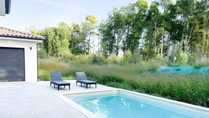 A swimming pool with two lounge chairs and a covered area, surrounded by greenery and trees. - Relaxation & Serenity in Coulounieix-Chamiers – House with Pool and Spa (Coulounieix-Chamiers)