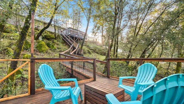 A wooden deck with two chairs and a bench, surrounded by trees and a wooden staircase leading to a building. - Serene Creek Escape | SPA•Arcade•Yosemite  •14 guest (Sonora)