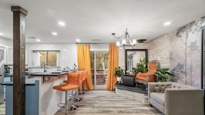 A modern kitchen with a bar area, a seating area with a sofa and chairs, and a view through a glass door. - Serene Creek Escape | SPA•Arcade•Yosemite•14 guest (Sonora)