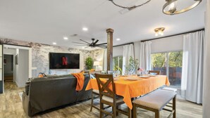 A dining area with a table set for four, a sofa, and a television mounted on the wall. - Serene Creek Escape | SPA•Arcade•Yosemite•14 guest (Sonora)