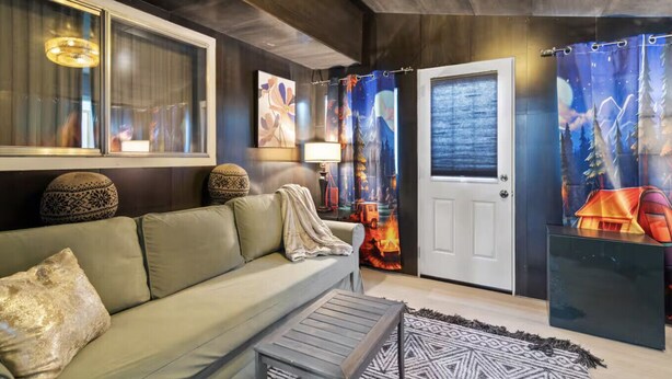 A modern living room with a sofa, a coffee table, a lamp, and a door with a forest-themed curtain. - Family Game Retreat|Spa•Arcade•Pickleball•Yosemite (Sonora)