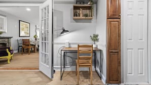A room with a desk, chair, open door, and a small shelf with decorative items. - Family Game Retreat|Spa•Arcade•Pickleball•Yosemite (Sonora)