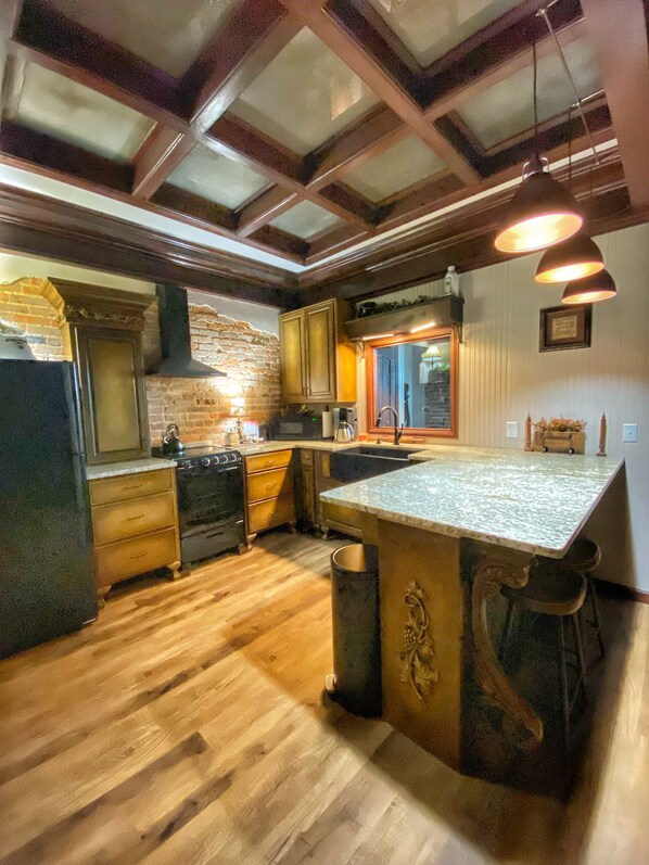 A kitchen with wooden floors, a large island, a brick wall, and pendant lighting.
