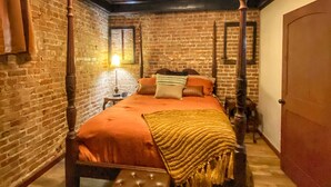 Una stanza con un letto a baldacchino, una ventola a soffitto e un muro in mattoni.