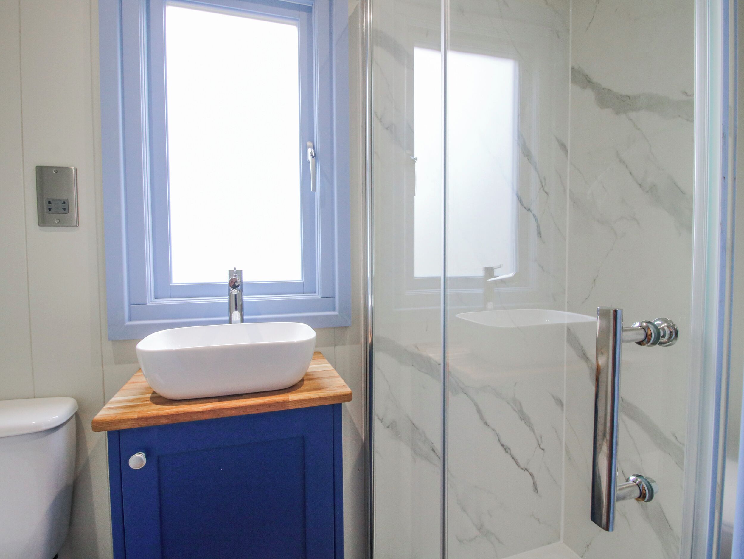 A bathroom with a white sink, blue cabinet, and a glass shower enclosure.