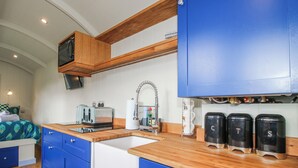 A compact kitchen with blue cabinets, a wooden countertop, a toaster, a kettle, and a sink. - Skye (Ludlow)